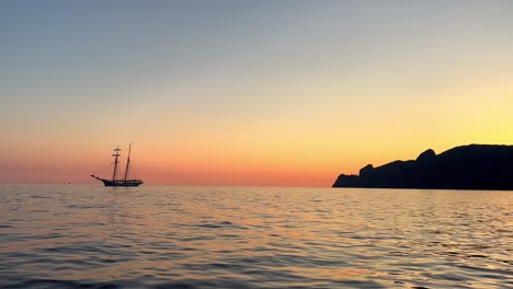backlight view of ancient sailing ship with lowered sails navigating at sunset or sunrise seen from moving boat