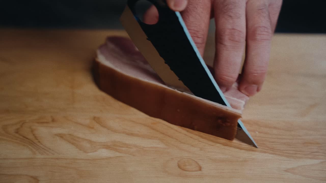 나무 절단판에 날카로운 칼로 흡연 된 햄을 잘라내는 손, 클로즈업