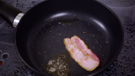 fried bacon in a pan in a slow-motion shooting