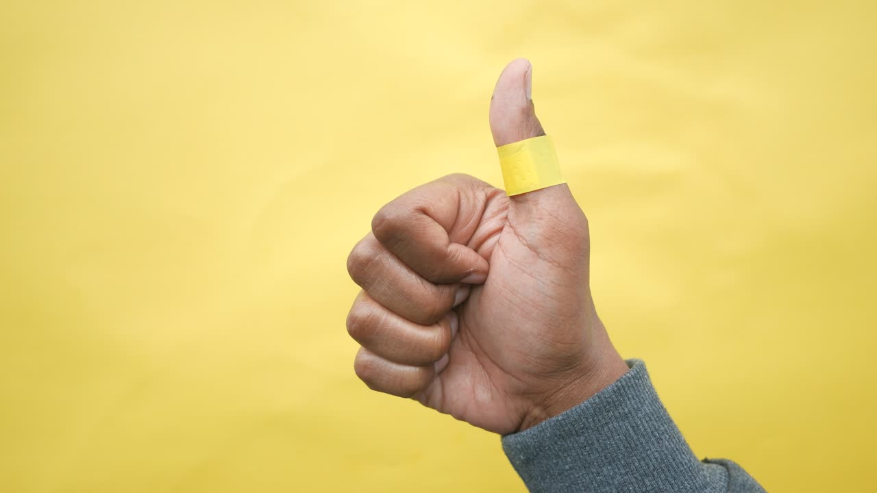 mano con los pulgares hacia arriba y vendaje amarillo