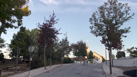 Static-shot-capturing-a-Lisbon-neighborhood-and-a-Catholic-church,-with-the-moon-overhead-in-the-backdrop,-creating-a-tranquil-scene-in-Portugal