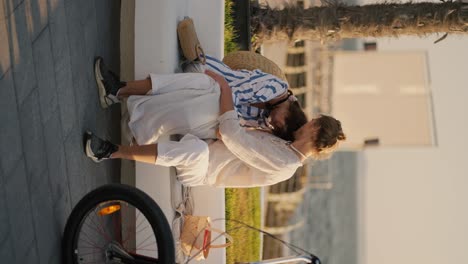 vertical video of a guy and a girl in beachwear sitting on a white bench on a modern beach and talking on their date near the sea. happy couple on a date on a pier near the sea