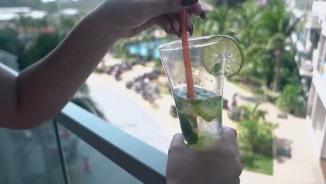 young-woman-holds-high-glass-in-hand-and-stirs-fresh-mojito