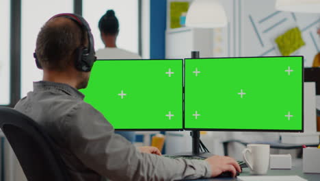 employee with headphones working in dual monitror setup with green screen