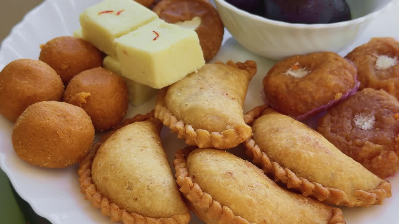 Close-up em plataforma giratória focando em gujiya crocante com bordas frisadas detalhadas, rodeado por doces indianos tradicionais como gulab jamun, laddu, peda e barfi, destacando texturas ricas e a atmosfera festiva.