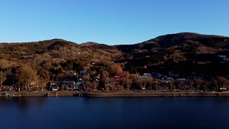 A-serene-lakeside-town-at-dusk-with-autumn-foliage,-aerial-view