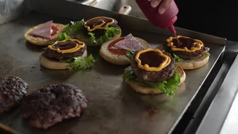 anonymous cook preparing tasty hamburgers and adding sauce