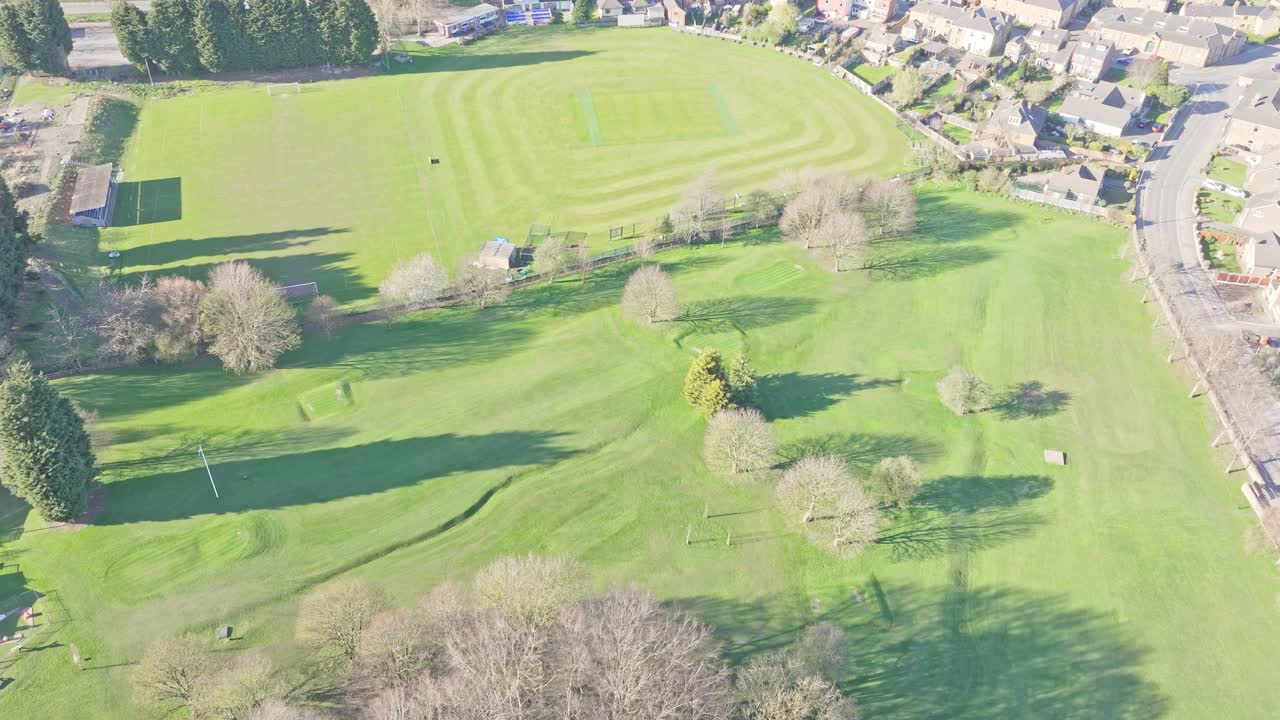 Lush green field with walking trail and trees in Elsecar Park, aerial dolly over fields