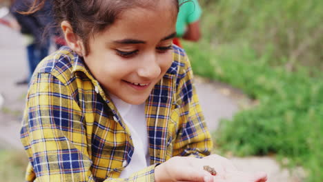 Mädchen-Hält-Kleinen-Frosch-Als-Gruppe-Von-Kindern-Im-Outdoor-Aktivitätscamp,-Um-Das-Leben-Im-Teich-Zu-Fangen-Und-Zu-Studieren