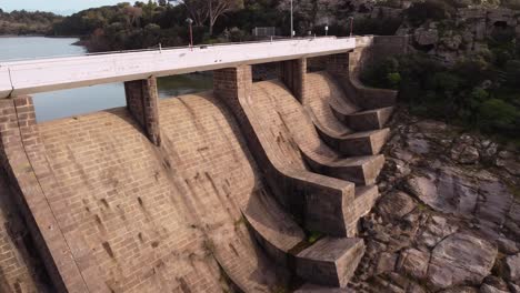 Stunning-aerial-view-of-Tratalias-Dam-rising-up-reveals-lake,-forward,-day