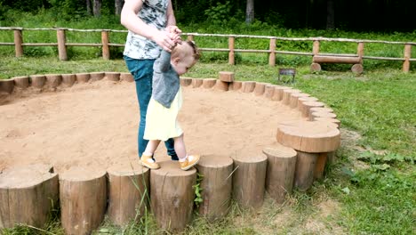 man in t-shirt and jeans helps toddler lady walk on stumps