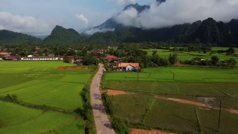 Coches-Que-Pasan-Por-Una-Carretera-Estrecha-En-Una-Zona-Rural-Con-Abundantes-Campos-De-Arroz-Y-Montañas-En-Laos.