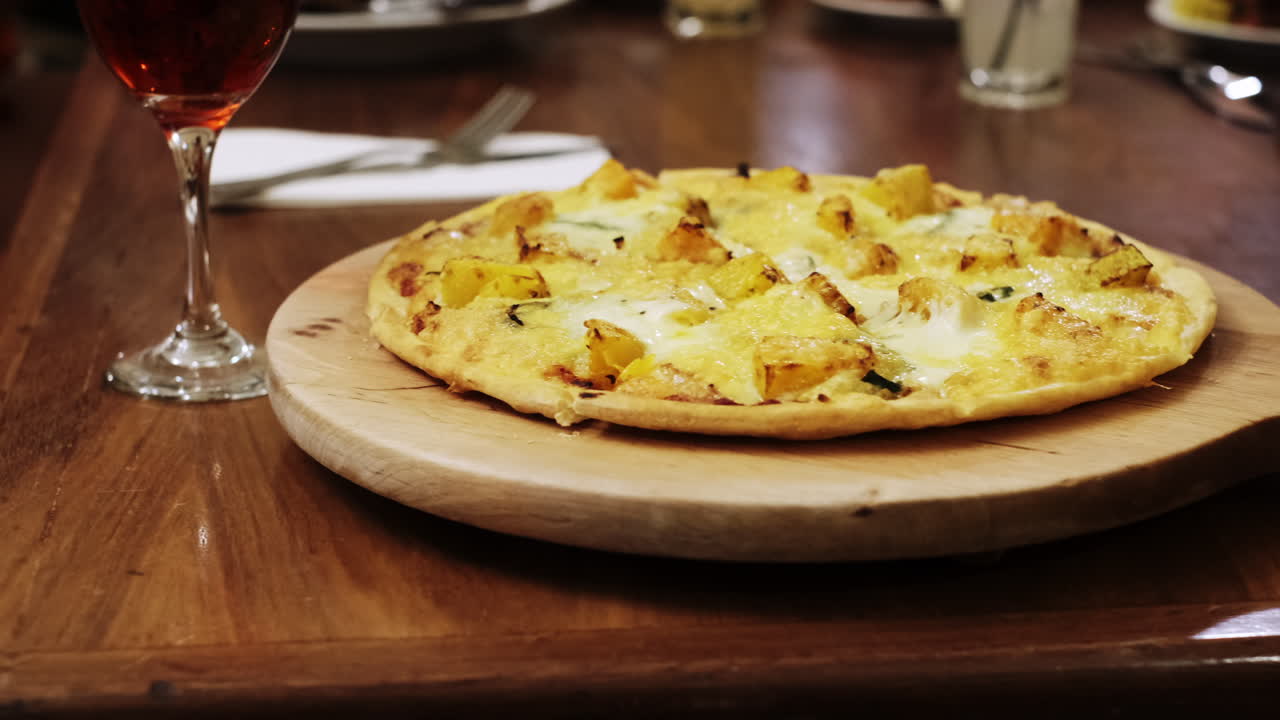 pizza hawaiana en tablero de madera y copa de vino