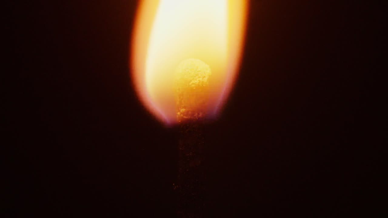 slow motion macro shot of a match head being ignited by fire and then burning until it extinguishes itself on a black background