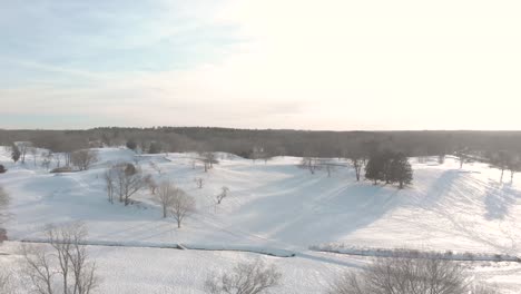 Un-Suave-Descenso-Para-Mostrar-El-Horizonte,-Un-Hermoso-Y-Tranquilo-Campo-De-Golf-Cubierto-De-Nieve,-Todo-A-Través-De-Drones