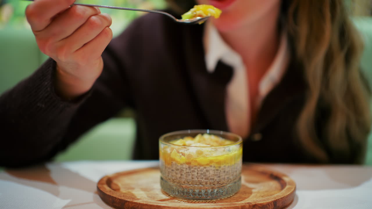 Femme mangeant un pudding au chia dans une tasse en verre avec une cuillère.