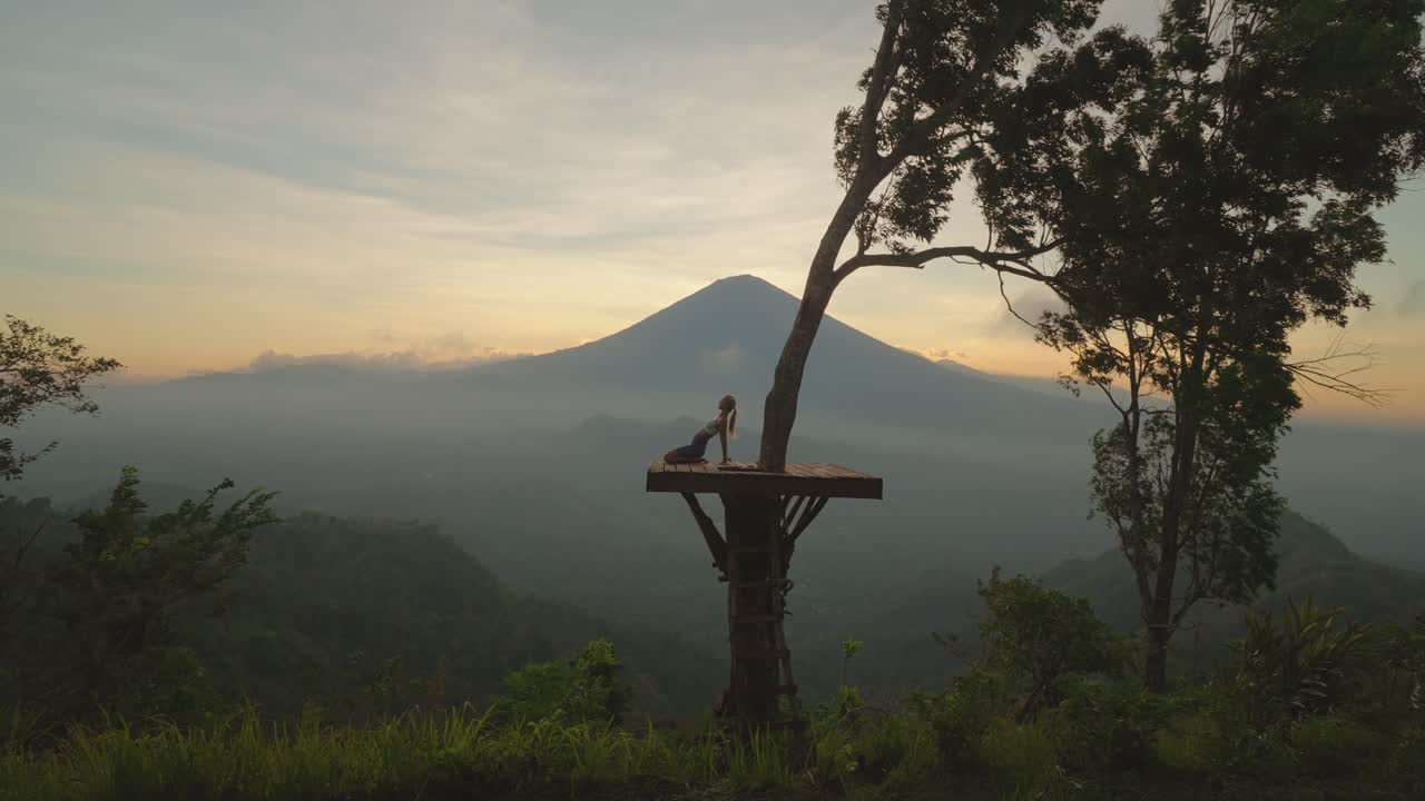 mujer doblándose hacia atrás en pose de camello en una plataforma de madera con vista mágica del monte agung, momento de zen