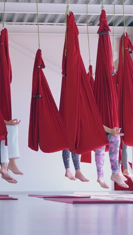 women group practices anti-gravity yoga meditation sitting relaxed in butterfly pose in special hammocks
