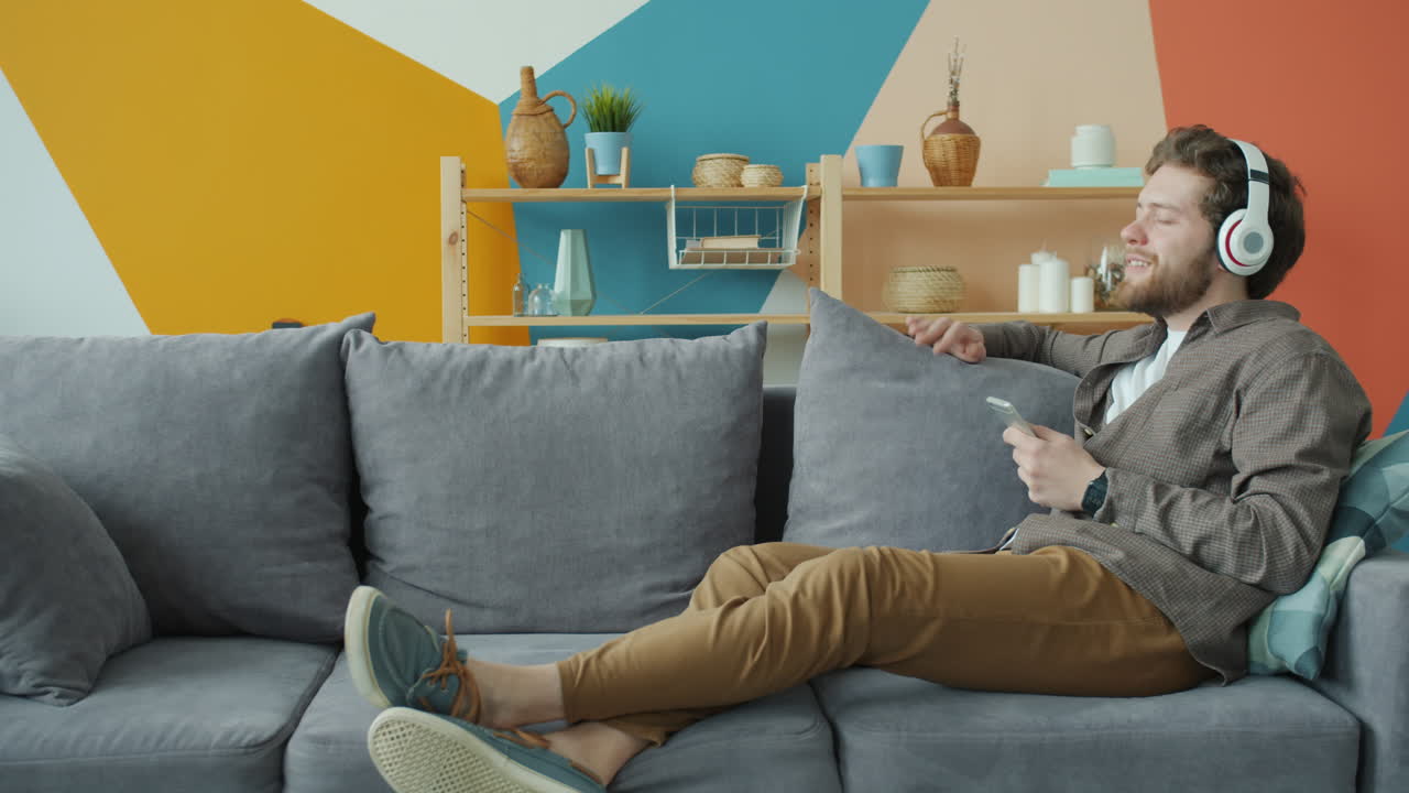 hombre relajándose en el sofá con auriculares y teléfono inteligente