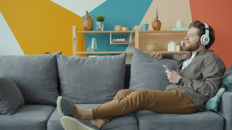 hombre relajándose en el sofá con auriculares y teléfono inteligente