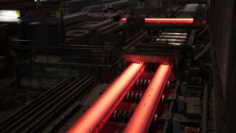 Glowing-steel-bars-cooling-on-conveyor-in-a-dark-industrial-setting,-overhead-view