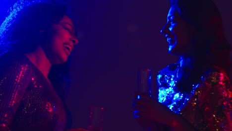 close up of two women in nightclub bar or disco talking and drinking alcohol