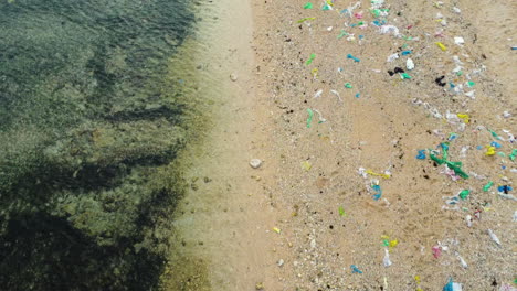 toma aérea de agua oceánica transparente y arena contaminada de la playa