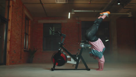 chica atlética hace trucos acrobáticos en bicicleta haciendo ejercicio en una máquina de ciclismo estacionaria en el interior