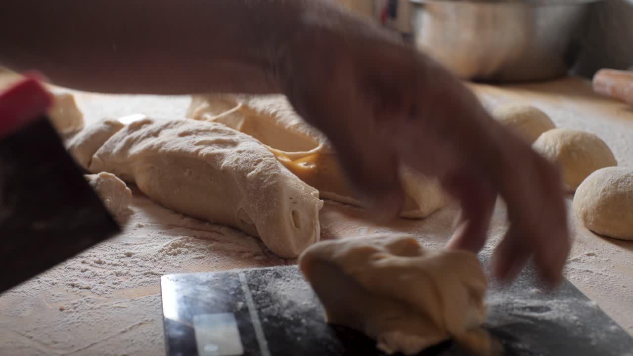 Skilled baker cutting bread dough into loaves to be baked, small home-based bakery business during COVID-19 pandemic