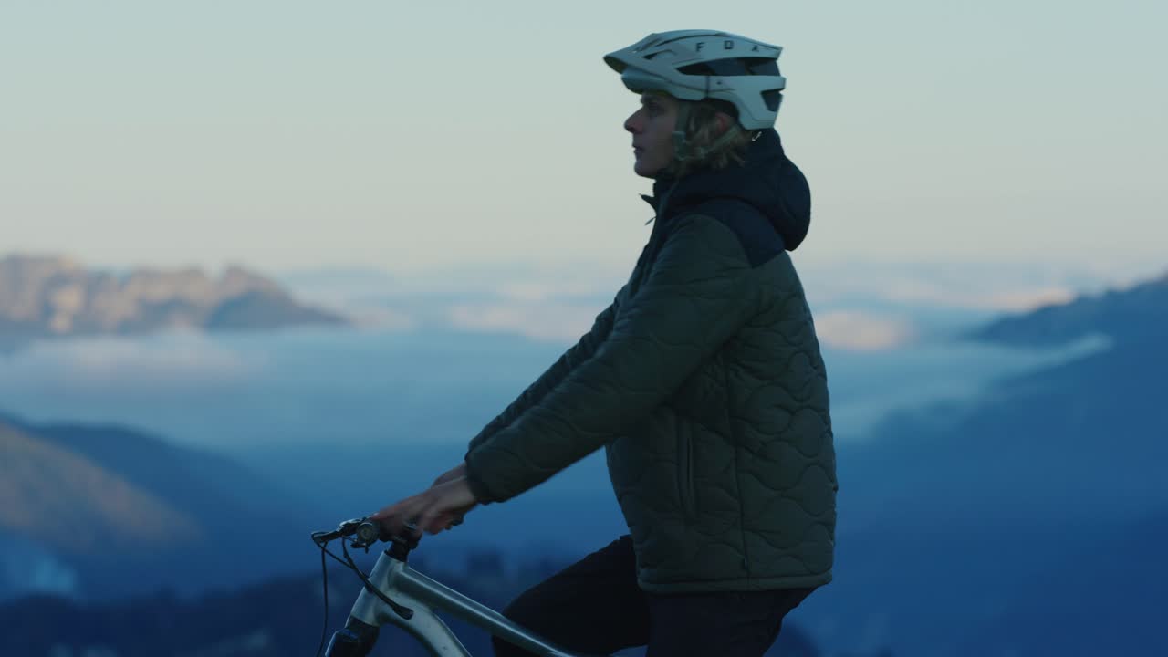 un ciclista de montaña descansa sobre un mar de nubes al atardecer