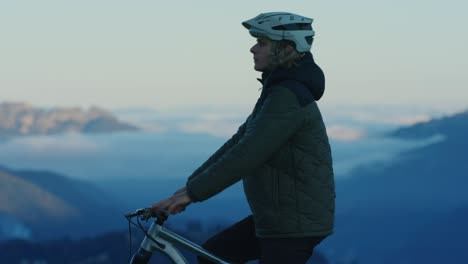 a mountain biker is resting above a sea of clouds at sunset