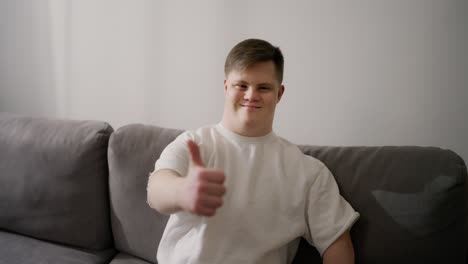 Young-adult-man-sitting-on-sofa,-happy-with-big-smile-doing-ok-sign,-thumb-up-with-fingers,-excellent-sign