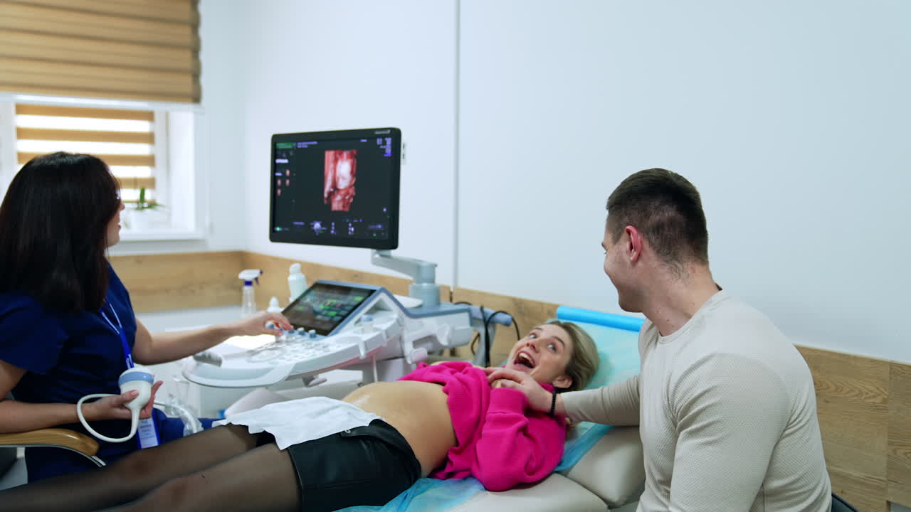 Husband and wife are smiling when they see ultrasonic scan image of their future baby. Doctor tells the child's gender and couple is excited.
