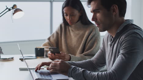 hombre de negocios trabajando en una computadora portátil en un escritorio colaborando con una colega usando un teléfono móvil