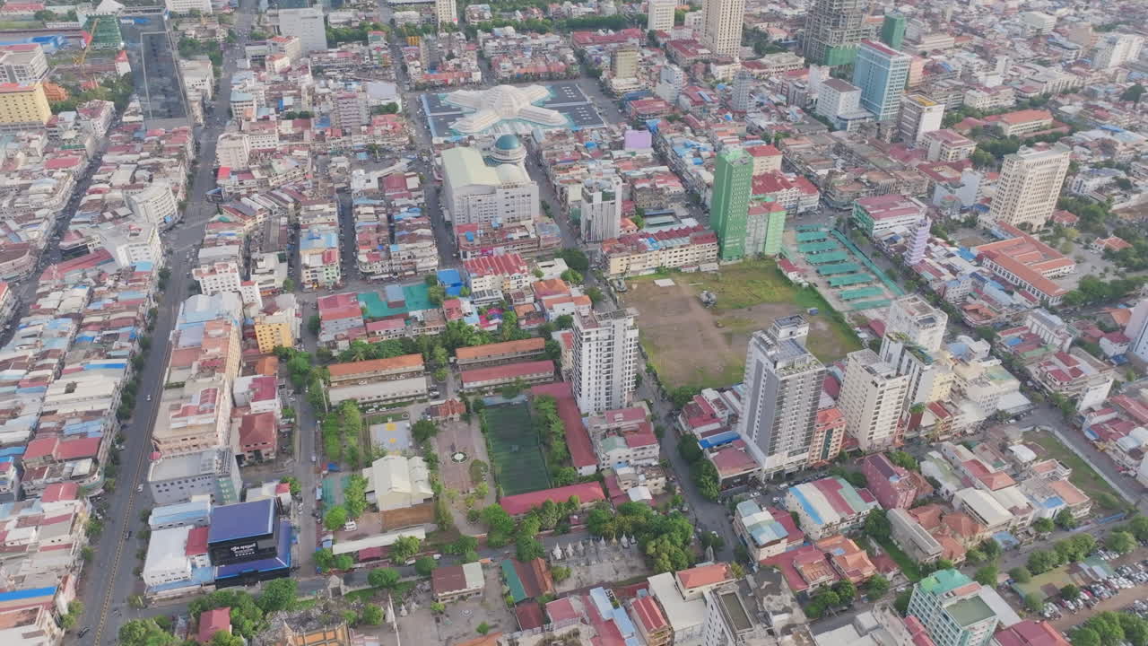 Top-down aerial video of Phnom Penh displays gridded city blocks, colorful rooftops, and narrow streets winding through low-rise buildings and mid-rise apartments