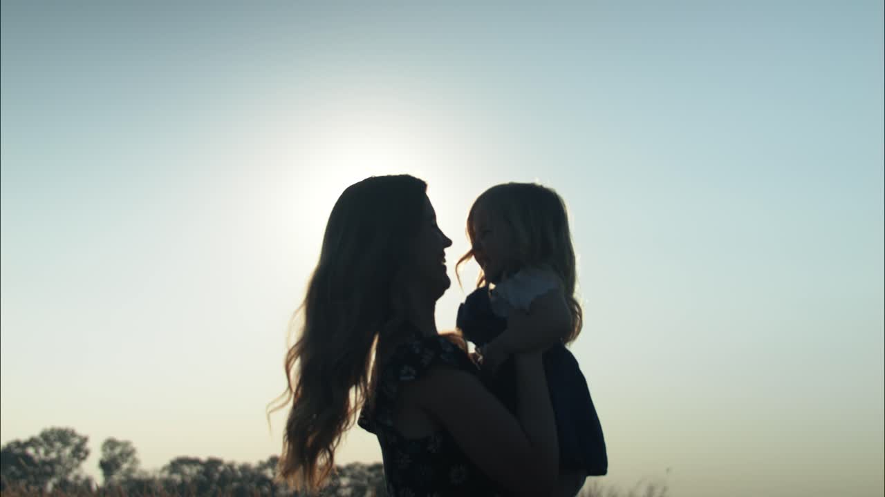 Silhouette di una madre e figlia felici che giocano, ridono, sorridono insieme all'aperto al tramonto estivo, vivendo un momento familiare positivo e affettuoso o un momento della festa della mamma in slow motion cinematografico