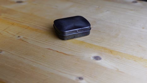 Small-silver-metal-box-lies-on-a-wooden-table-and-rotates-with-dark-me-behind