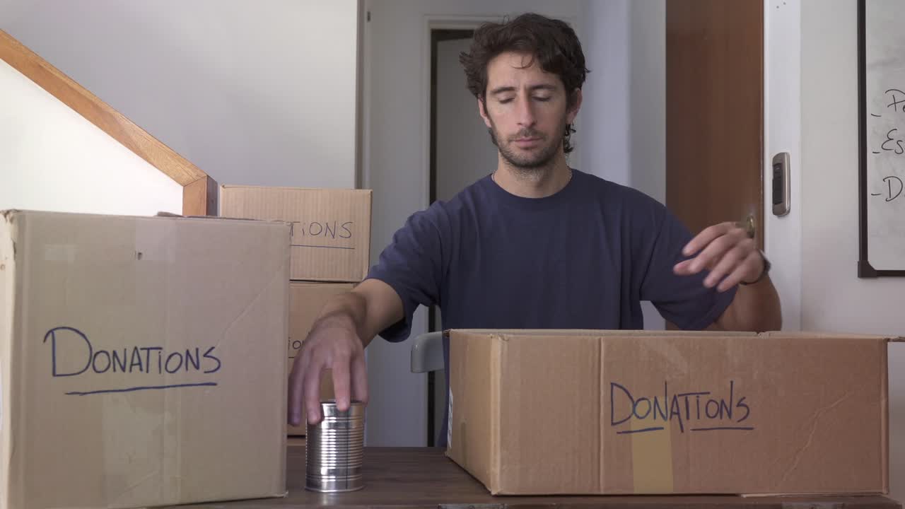 Homem embalando alimentos enlatados em caixa de doação e fazendo sinal de positivo