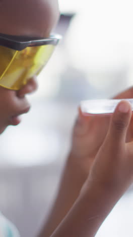 video de un feliz niño afroamericano con gafas y con reactivo en la mano durante la lección de química