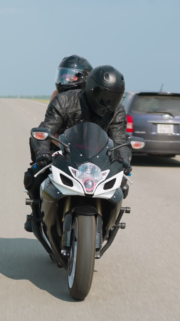 Biker with girlfriend ride contemporary motorcycle together along road past empty field at countryside on sunny spring day slow motion