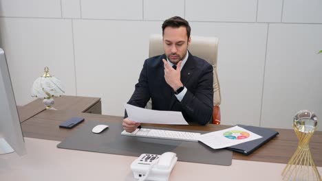 busy thoughtful european businessman analyzing financial documents and checking data while sitting at a workplace desk in a business office. financier deals with financial report - parallax shot