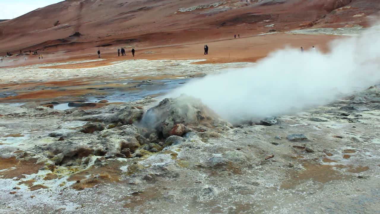 연기가 나는 화산 간헐천, 배경에 사람과 모래 갈색 산이 있는 풀 hd