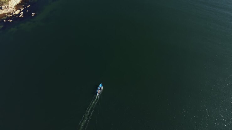 Una barca viaggia in acque aperte vicino alla riva durante una giornata limpida senza punti di riferimento visibili.