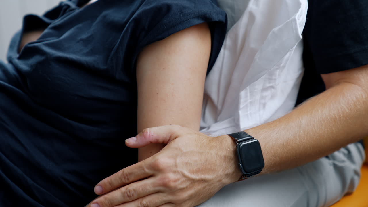 Unrecognized Caucasian couple sitting close to each other. Male hand stroking female shoulder comforting her. Pregnancy and delivery concept.
