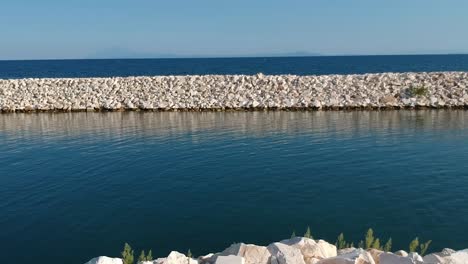 Aerial-drone-shot-of-a-wave-breaker-in-a-sunny-day-overlooking-the-mediterranean-ocean-in-Kavala-Greece