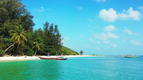 Ruhiger-Tropischer-Strand-Mit-Weißem-Sand-Und-Palmen,-Smaragdgrünes-Meerwasser-Mit-Schwimmenden-Booten