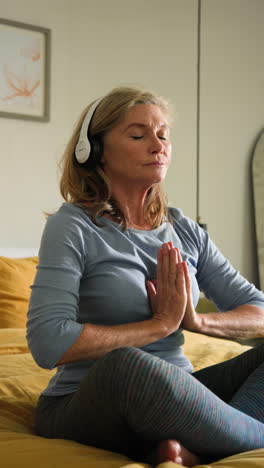 vertical video: senior woman meditating with headphones on bed, finding peace at home