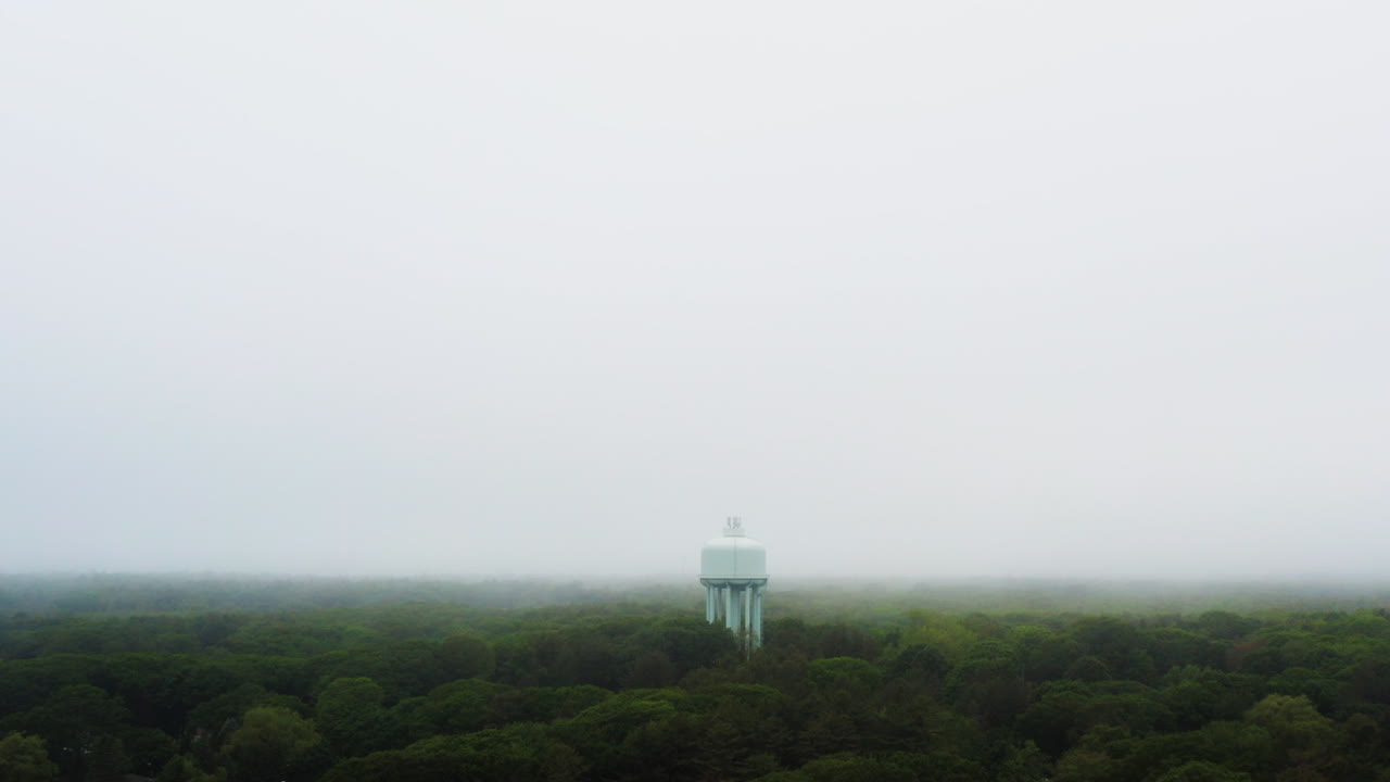 Drone shot of town water tower above green trees with low visibility foggy weather HD 30p