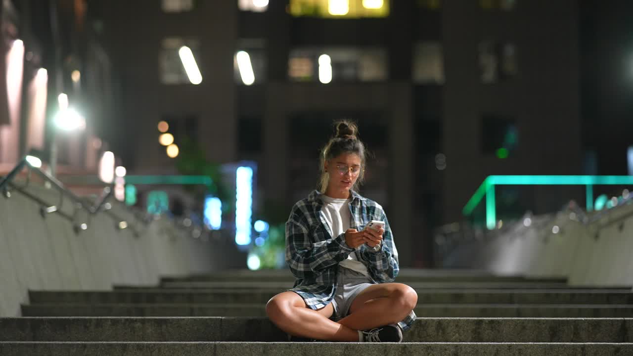joven usando un teléfono inteligente por la noche en las escaleras de la ciudad