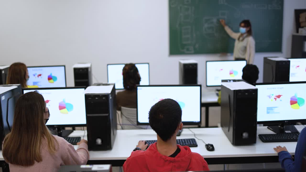 Multiracial young students and teacher wearing safety face masks during coronavirus outbreak inside computer class room at university